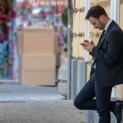 Business suited man with ear plugs looking at his phone outside Business suited man with ear plugs looking at his phone outside